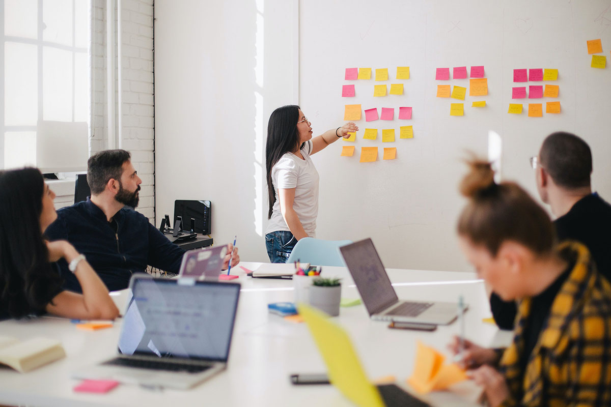 woman at whiteboard filled with sticky notes in meeting room