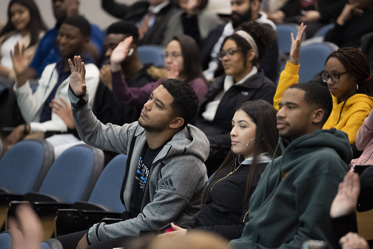 students sitting in auditorium with hands raised